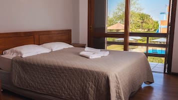 A bedroom with a large bed, wooden headboard, and a view of an outdoor swimming pool through a sliding glass door.