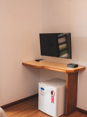 A compact room with a wooden desk, a flat-screen TV, and a small white refrigerator. - Sítio Hotel e Eventos (Sao Pedro do Sul)