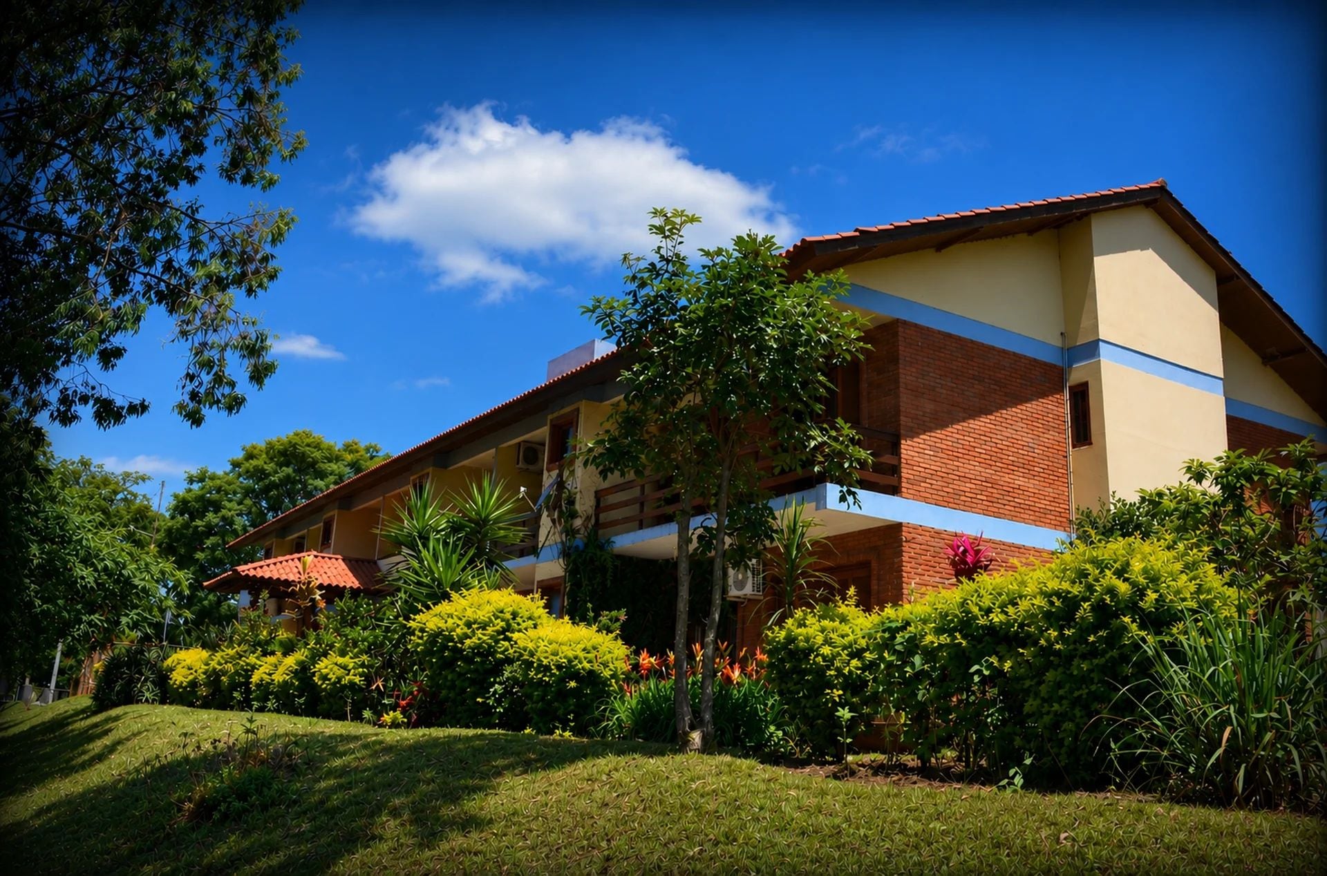 A two-story building with a flat roof, surrounded by lush greenery and a clear blue sky.