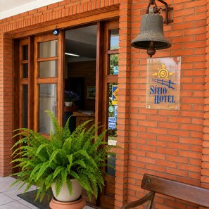 A hotel entrance with a large potted fern, a bell, and a sign for the Sìtio Hotel. - Sítio Hotel e Eventos (Sao Pedro do Sul)