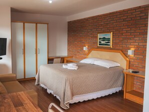 A bedroom with a bed, a wooden headboard, a brick wall, a painting, and a television on the wall. - Sítio Hotel e Eventos (Sao Pedro do Sul)