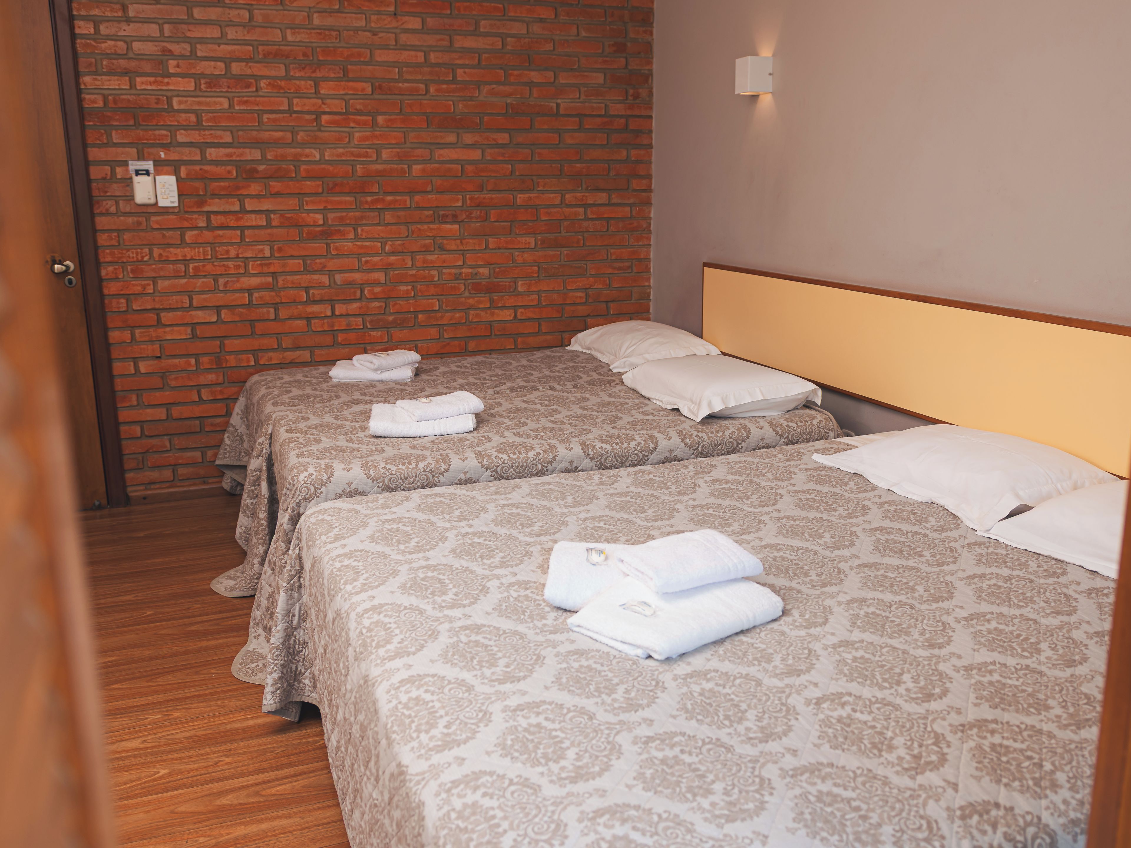 Hotellihuone, jossa on kaksi sänkyä, ja jokaisessa sängyssä on kuviollinen päiväpeite ja tyynyjä, sekä tiiliseinä.