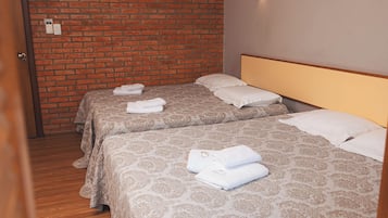 Hotellihuone, jossa on kaksi sänkyä, ja jokaisessa sängyssä on kuviollinen päiväpeite ja tyynyjä, sekä tiiliseinä.