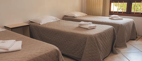 A hotel room with two beds, each with a quilted bedspread and a folded towel on top. There is a nightstand with a lamp, and the room has a window with blinds.