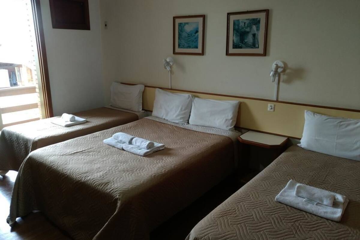A hotel room with two beds, each with a brown quilt and white pillows. There are two framed pictures on the wall above the beds.