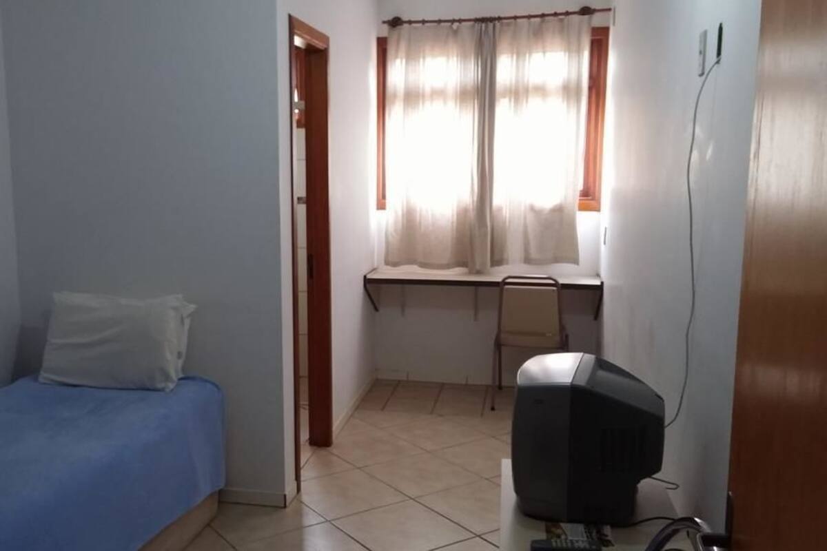 A small, sparsely furnished room with a single bed, a desk, and a television.