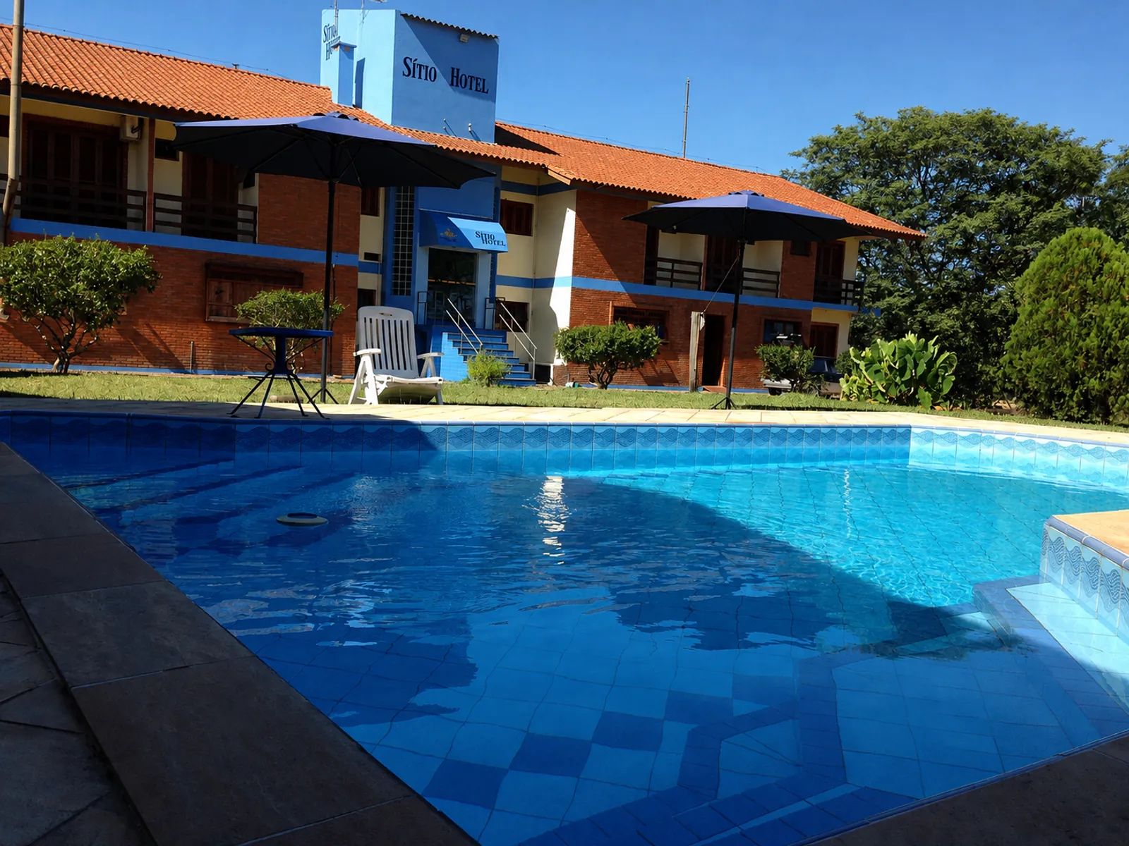A hotel with a swimming pool, outdoor seating, and a staircase leading to the entrance.