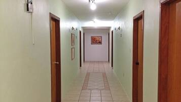 Um corredor com piso de azulejos, portas de madeira e luminárias fixadas na parede.