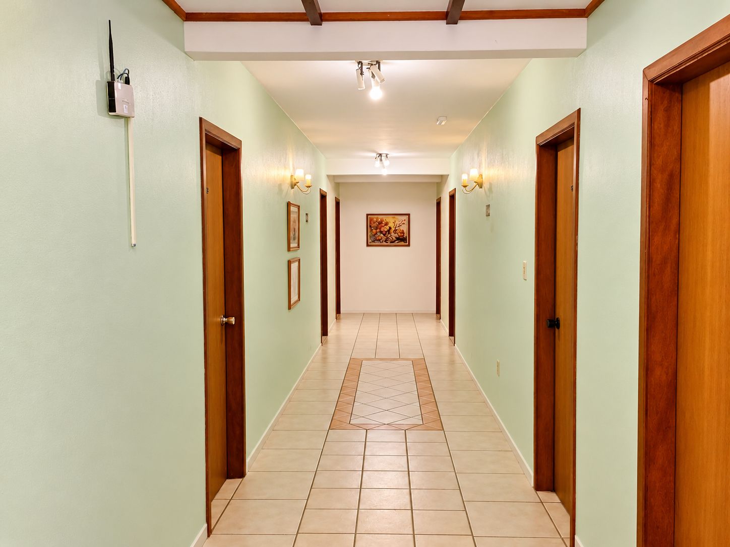 A hallway with wooden doors, light green walls, and a tiled floor.