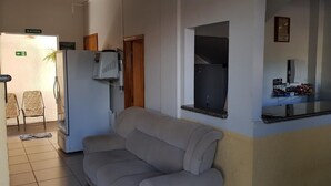 A reception area with a sofa, a refrigerator, a TV, and a counter with a computer and some items on it. - Hotel Guima (Santa Vitoria)