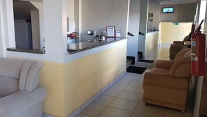 A reception area with a counter, a sofa, and a fire extinguisher. - Hotel Guima (Santa Vitoria)