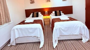 A hotel room with two beds, a radiator, a wooden headboard, a patterned carpet, and a wall-mounted artwork. - RBS Hotel, Rochester (Rochester)