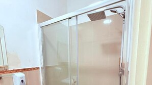 A glass-enclosed shower with a handheld showerhead, a white sink, and a hand soap dispenser. - RBS Hotel, Rochester (Rochester)