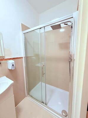 A glass-enclosed shower with a handheld showerhead, a white sink, and a hand soap dispenser.