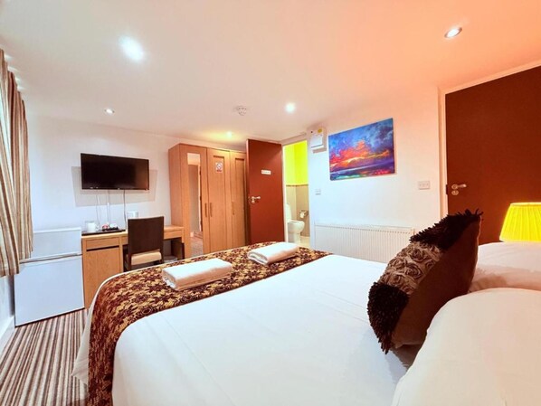 A hotel room with a bed, a desk, a television, and a bathroom visible through an open door.