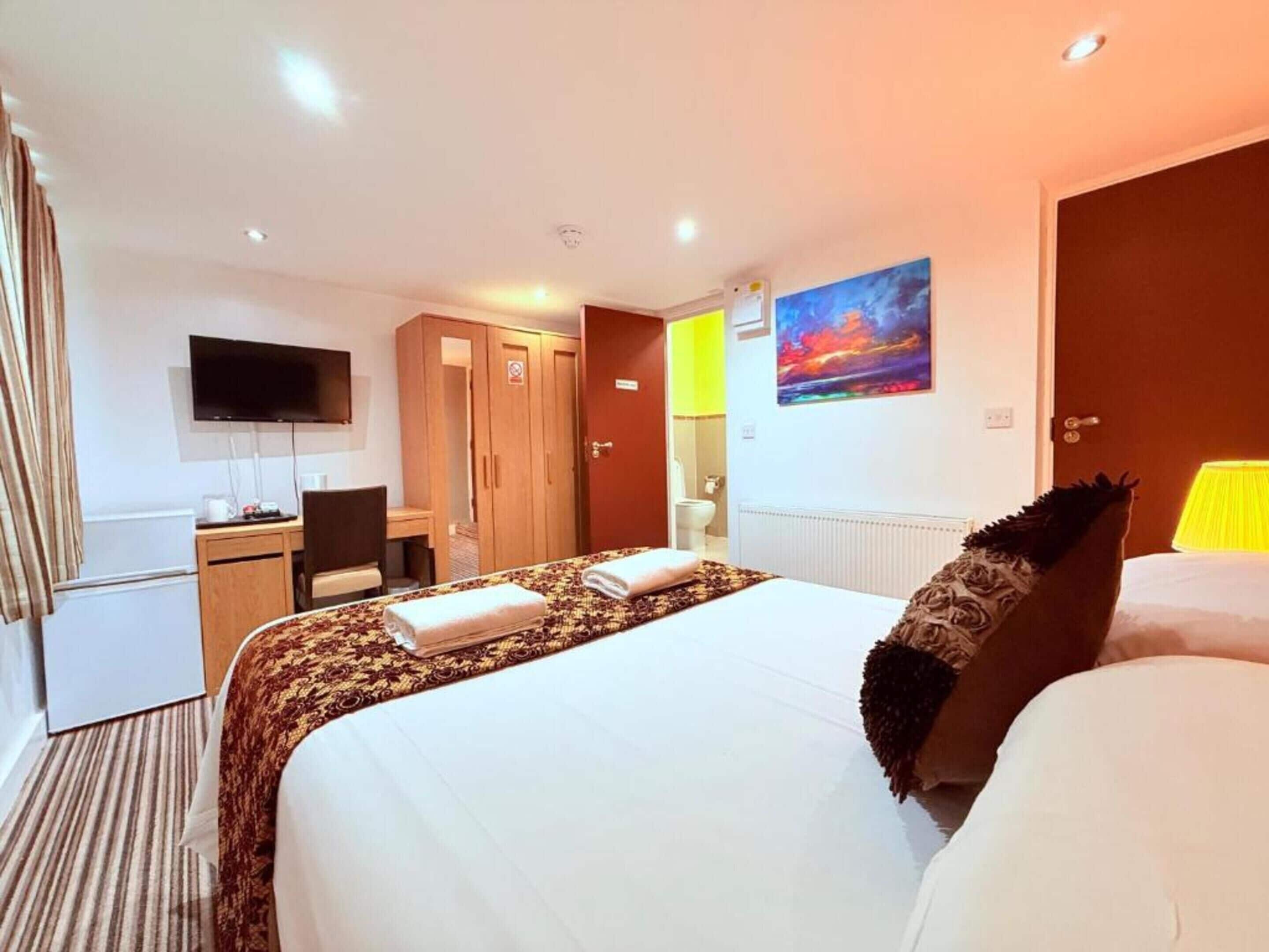 Une chambre d’hôtel avec un lit, un bureau, une télévision, une armoire et un tableau au mur.