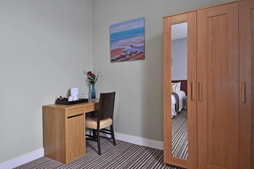 A hotel room with a wooden desk, a chair, a bed, and a painting of a beach scene.