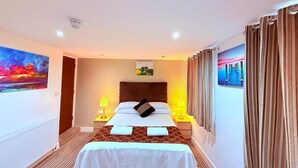 Une chambre d’hôtel avec un lit, deux tables de chevet avec des lampes, une tête de lit, un tableau au mur et un rideau.