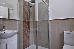 Casa de banho com chuveiro em cabine de vidro, lavatório branco e sanita.