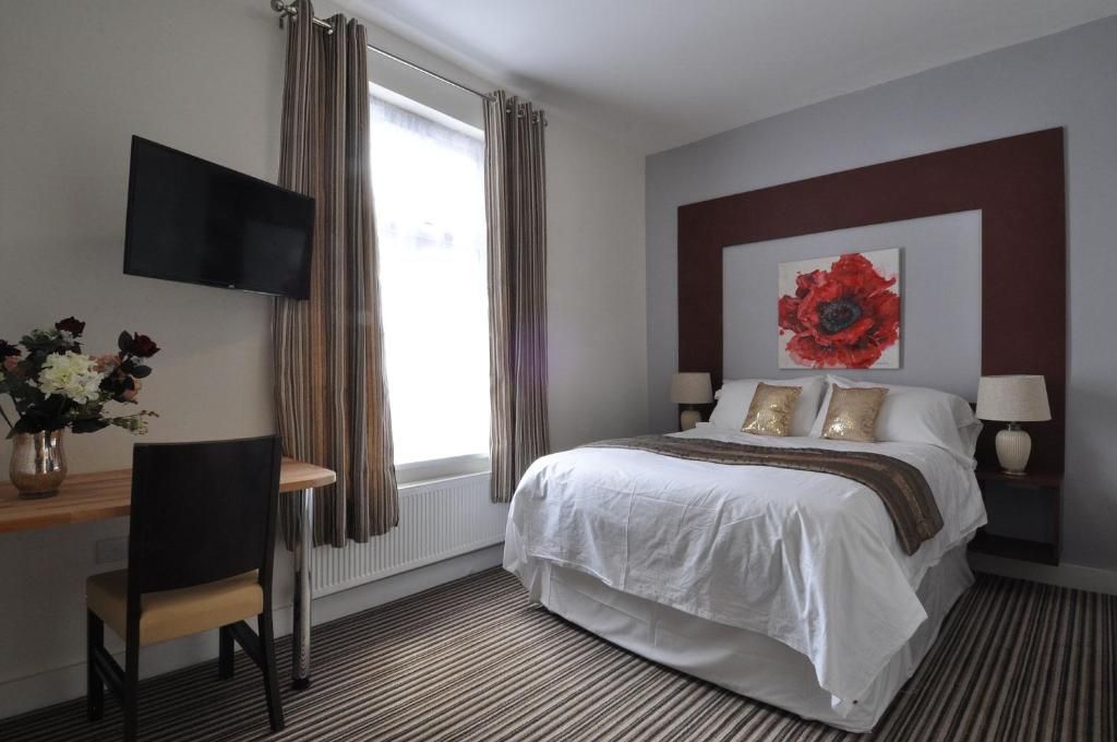 A hotel room with a bed, a TV, a desk, and a window with curtains.
