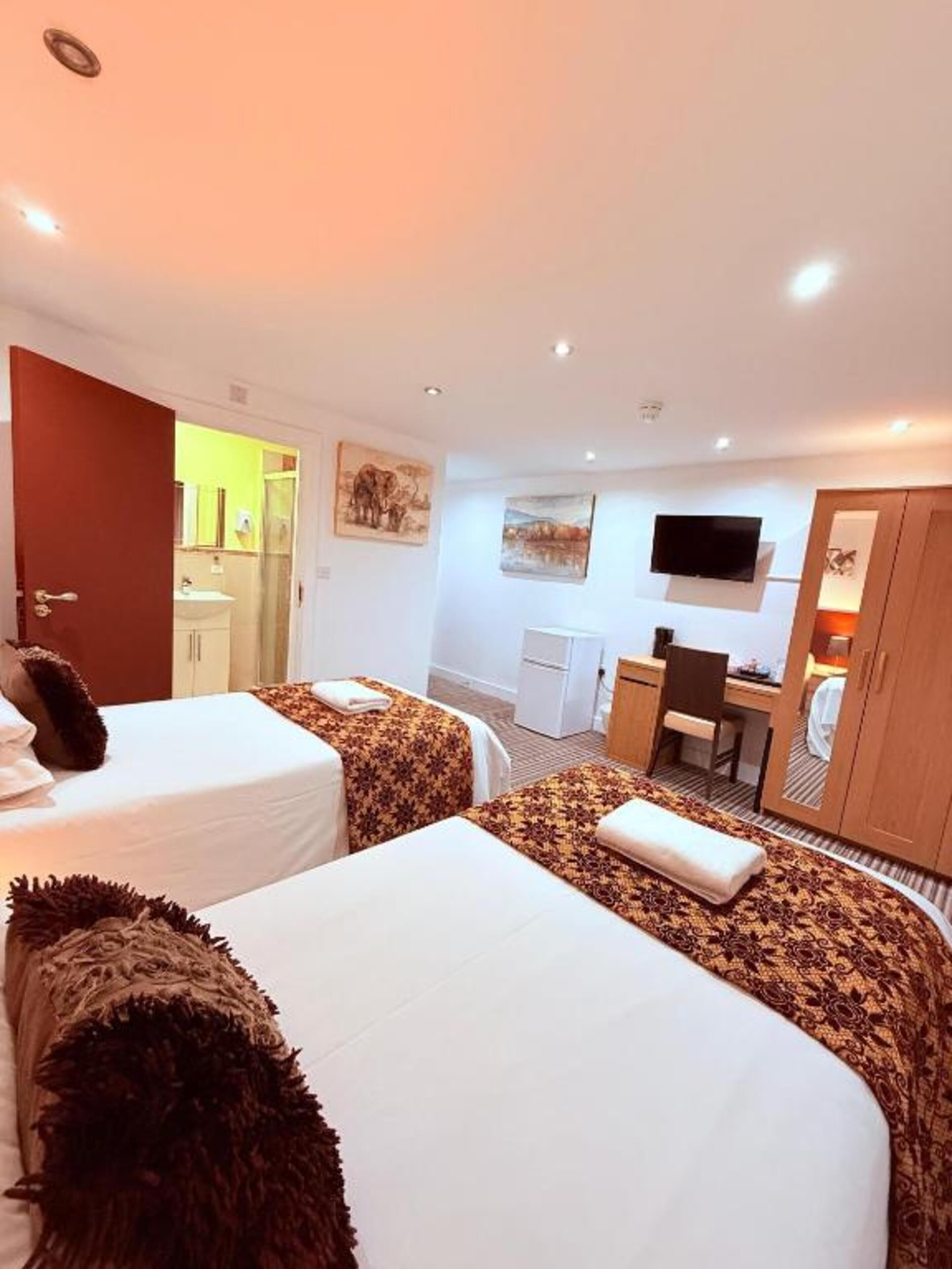 A hotel room with two beds, a desk, a TV, and a bathroom visible through an open door.
