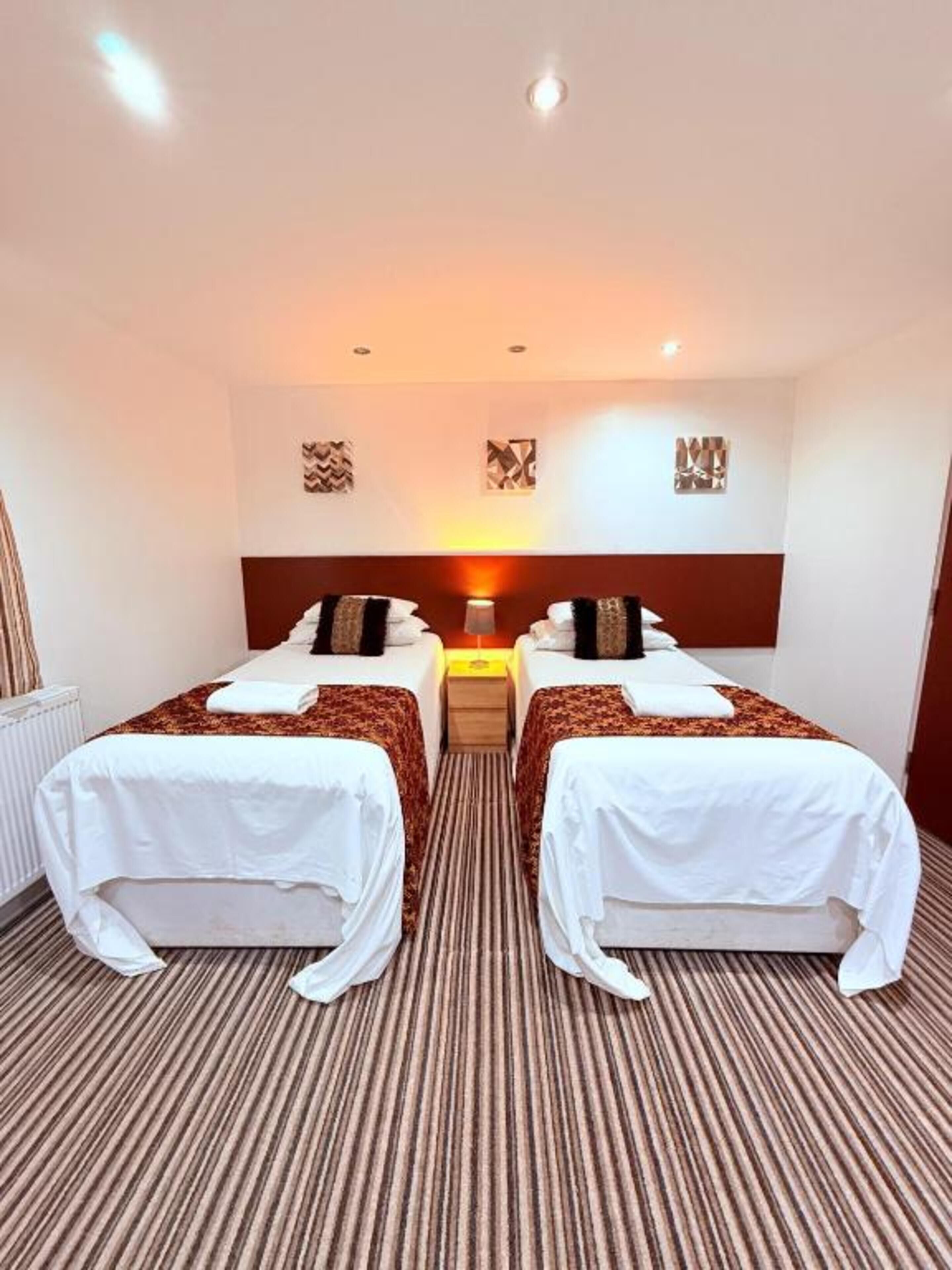 A hotel room with two beds, a central nightstand, and a radiator.