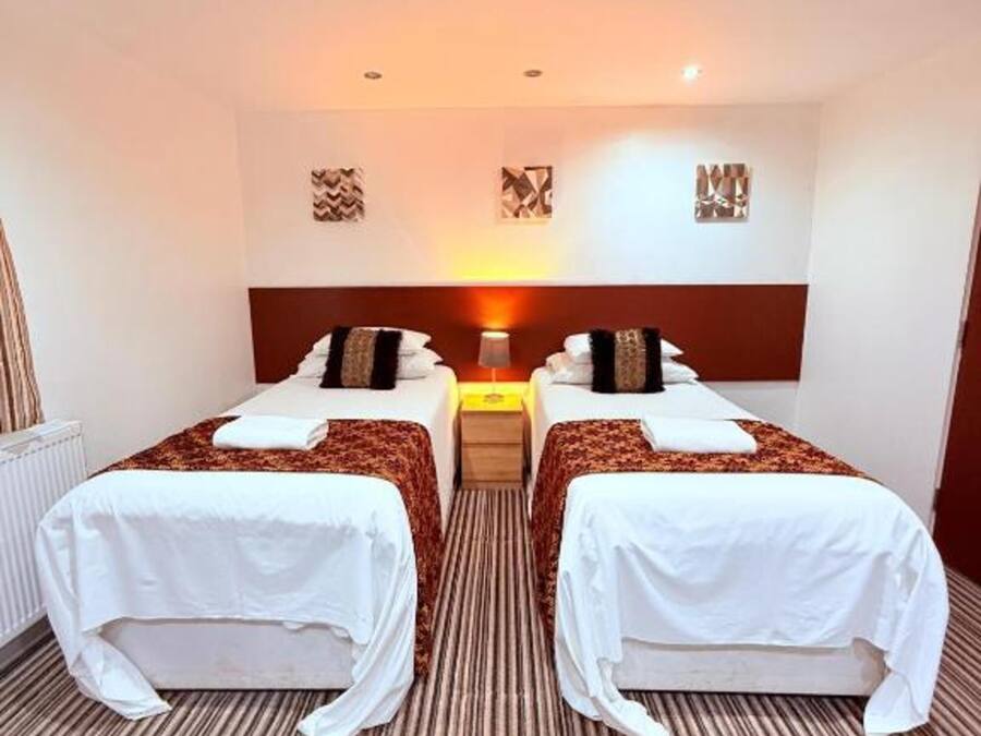 A hotel room with two beds, a central nightstand, and a radiator.