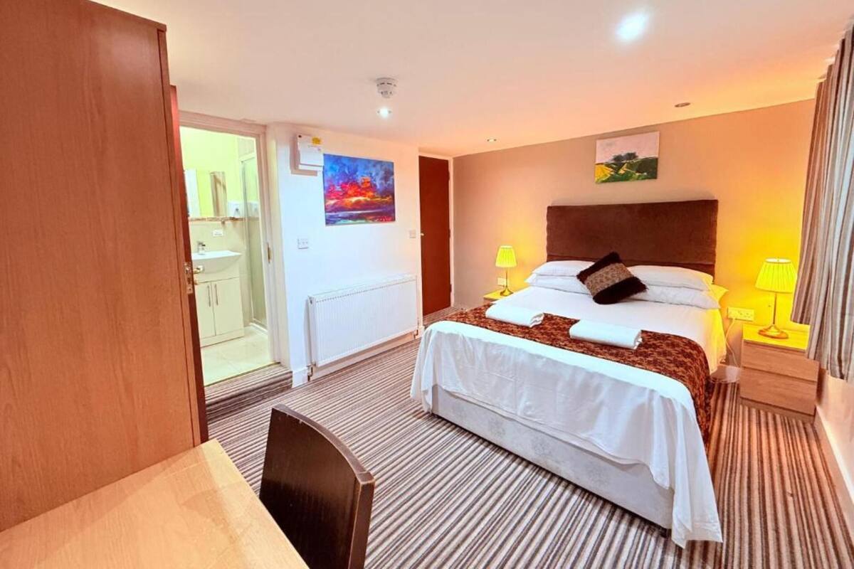 A hotel room with a bed, bedside lamps, a painting, a radiator, and a door leading to a bathroom.