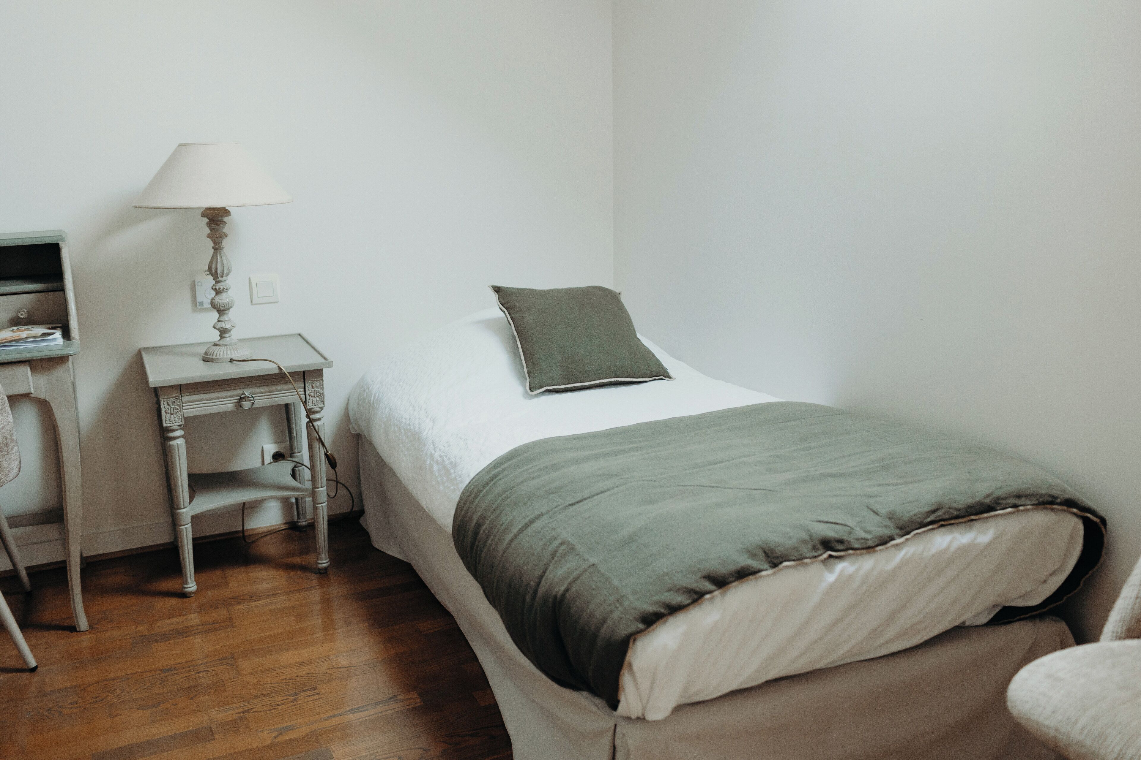 A bedroom with a bed, a nightstand, a lamp, and a desk.