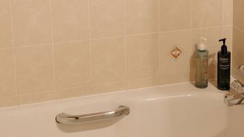 A bathroom with a bathtub, a handrail, and two bottles of Zenna body wash on the wall.