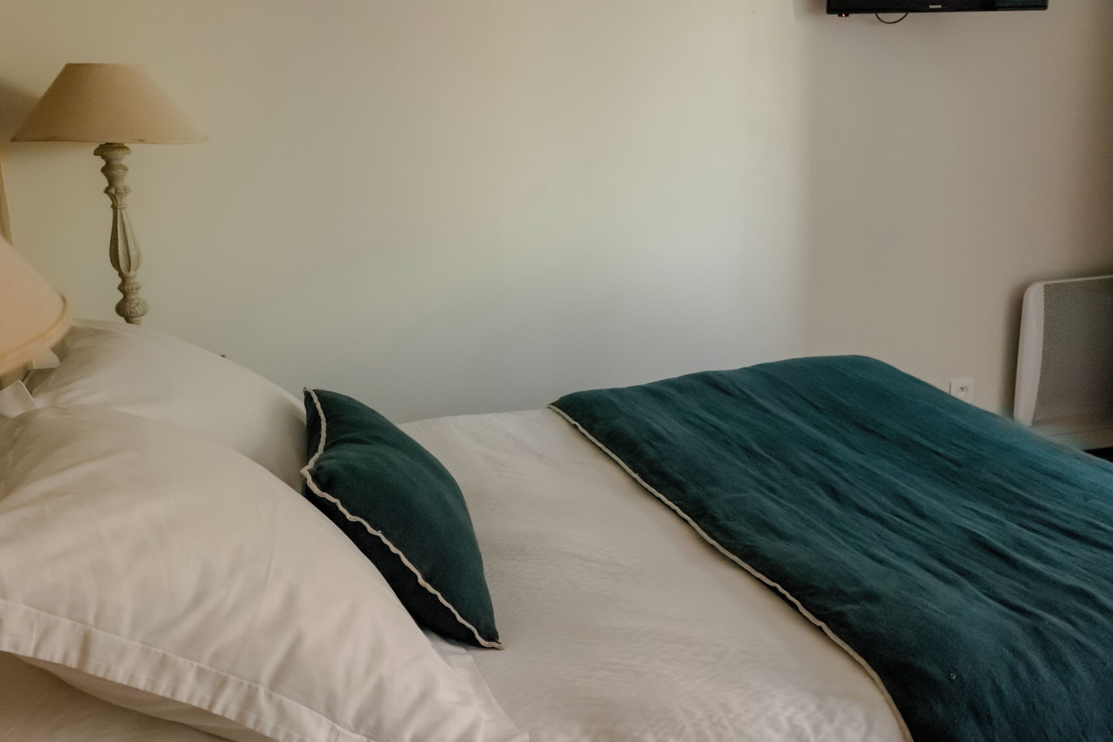 A bed with white and teal bedding, a lamp, and a wall-mounted air conditioner.