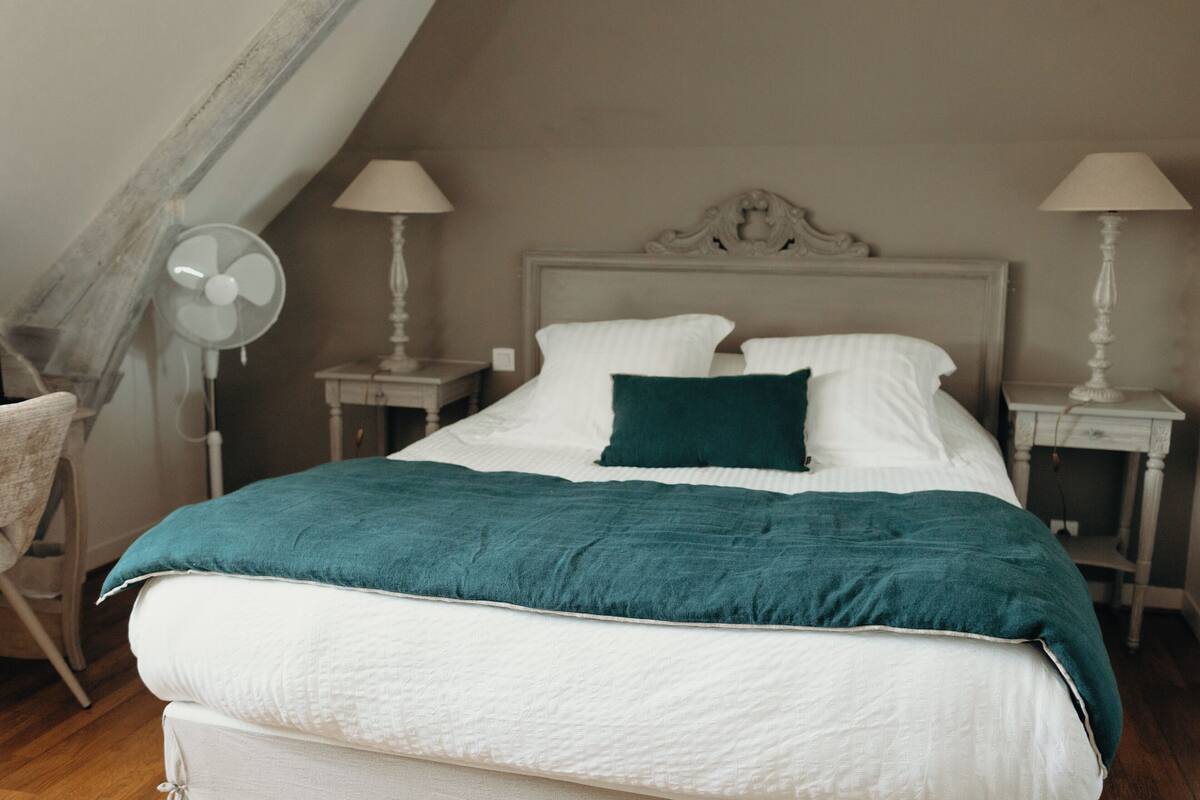 A neatly made bed with white and teal bedding, two bedside tables with lamps, and a chair.