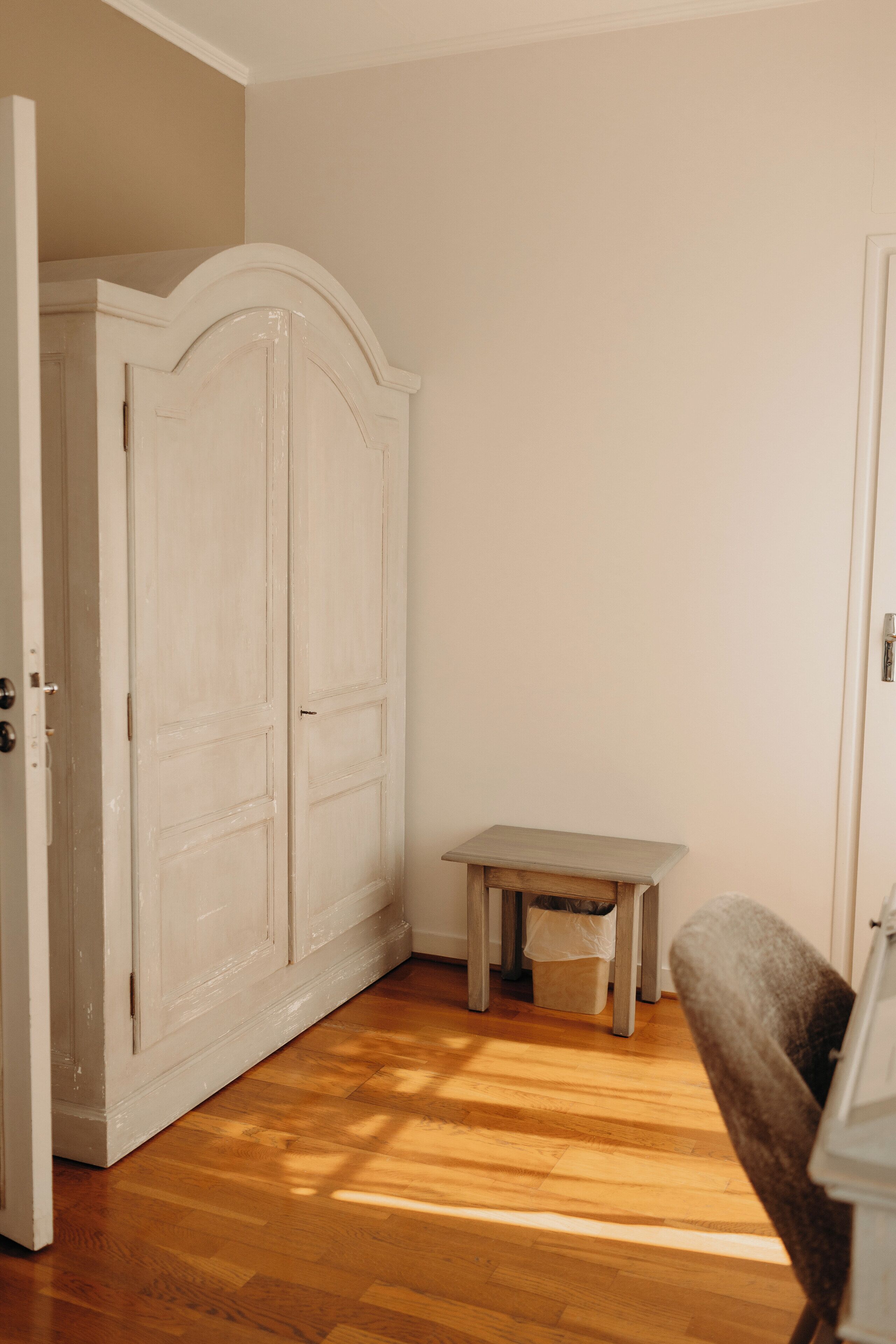 A room with a wooden floor, a white wardrobe, a small table, and a chair.