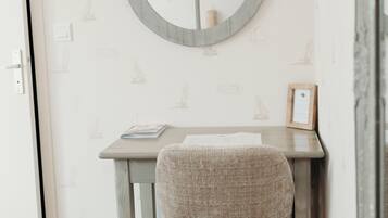 Una habitación con un espejo redondo en la pared, una mesita con una silla y un papel tapiz estampado.
