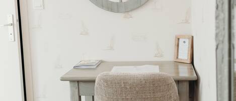 Una habitación con un espejo redondo en la pared, una mesita con una silla y un papel tapiz estampado.