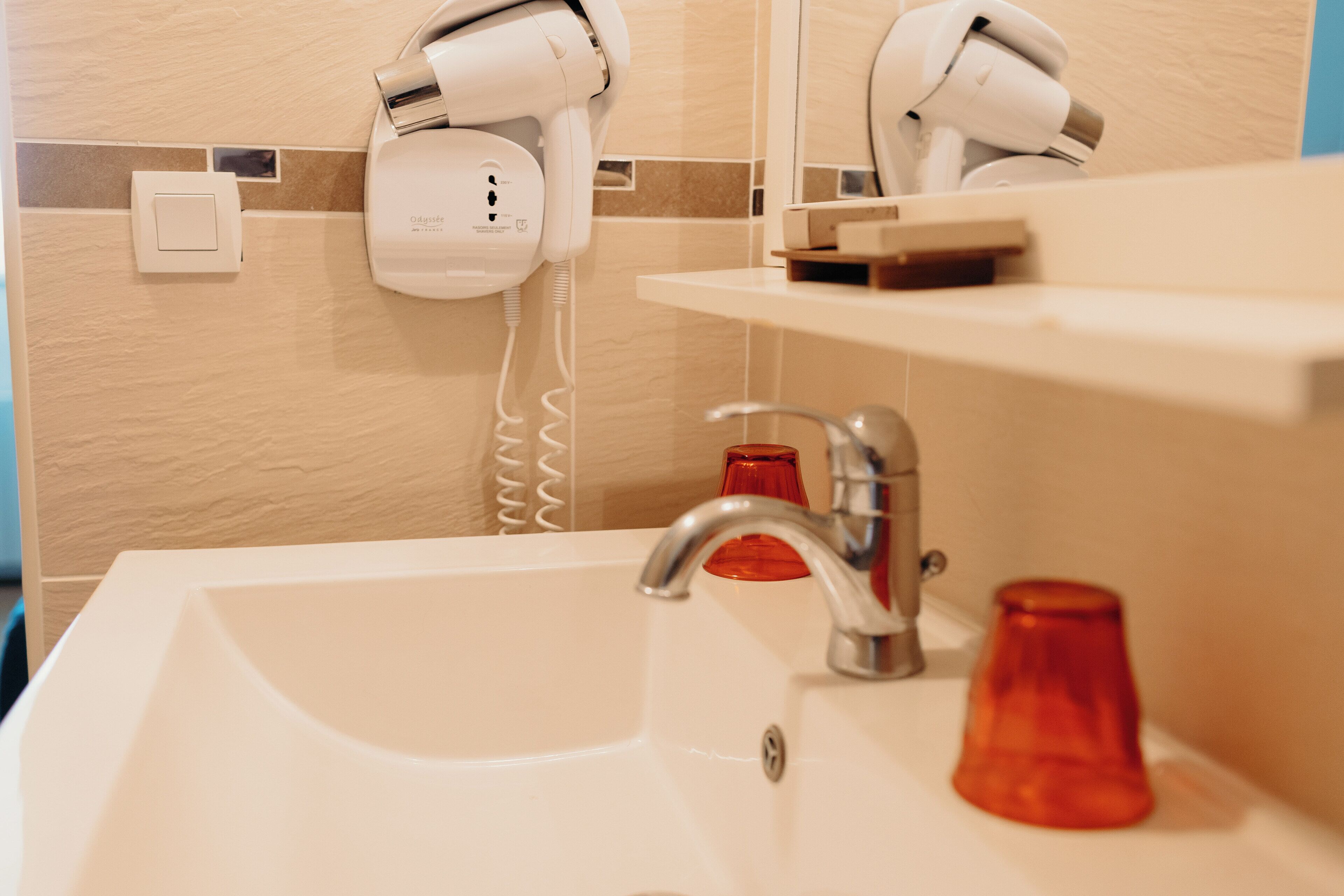 Un lavabo de salle de bain avec un miroir, un sèche-cheveux et un récipient en verre rouge.