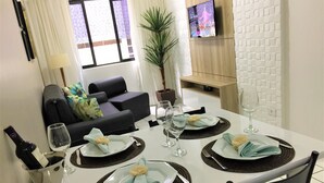 Una mesa de comedor preparada con platos, vasos y una botella, en una habitación con un sofá y un televisor.