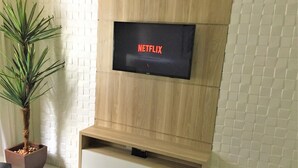 Televisor de pantalla plana montado en una pared de madera con el logotipo de Netflix, una planta en maceta y un piso con baldosas blancas.