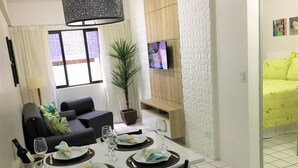 Un comedor con una mesa preparada para cuatro, un sofá, una planta en maceta y un televisor montado en la pared.