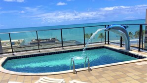 Piscina con fuente de agua, dos sillas de descanso y vista al océano.