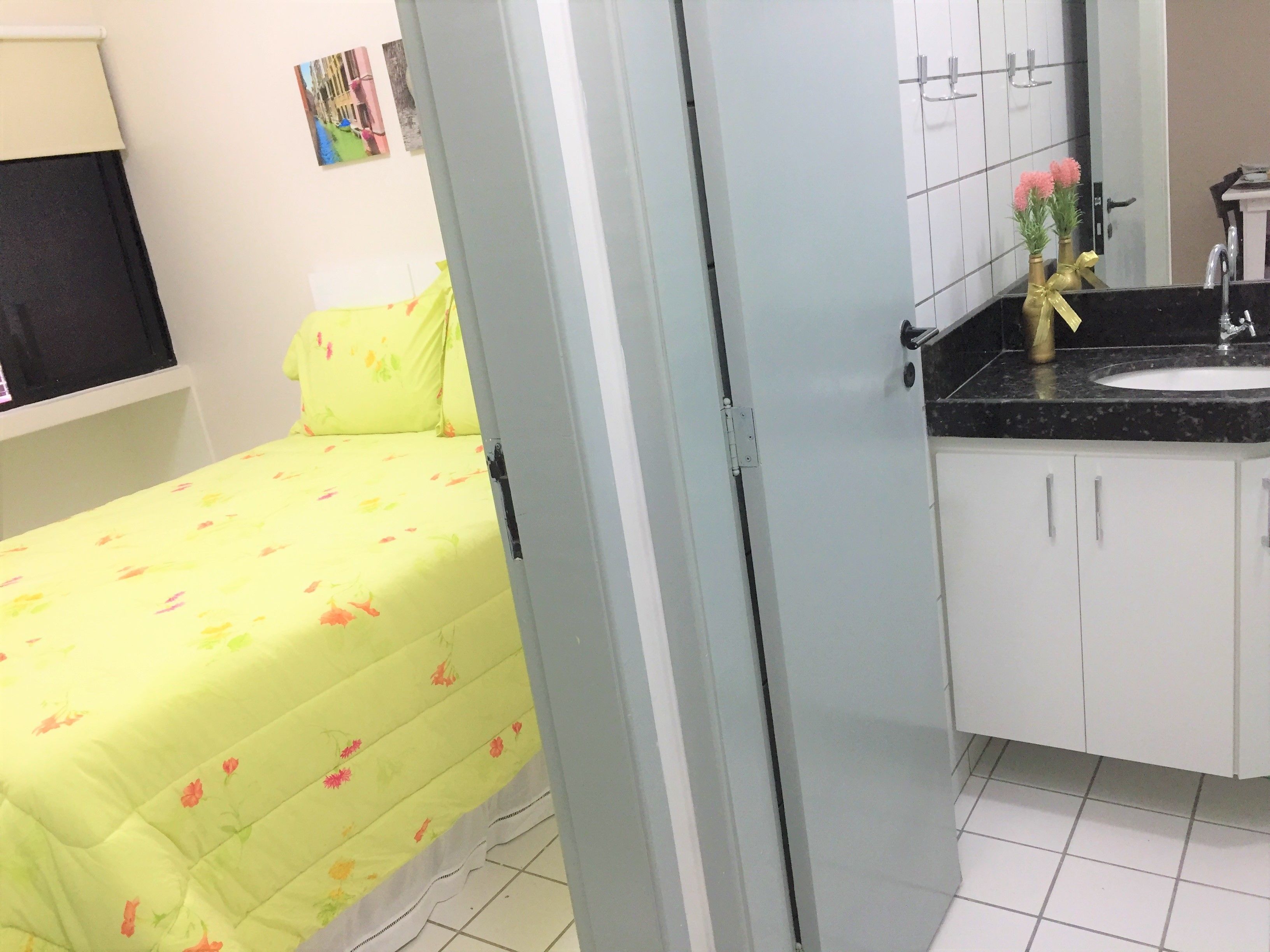 A room with a bed, a bathroom with a sink and mirror, and a door leading to another room.