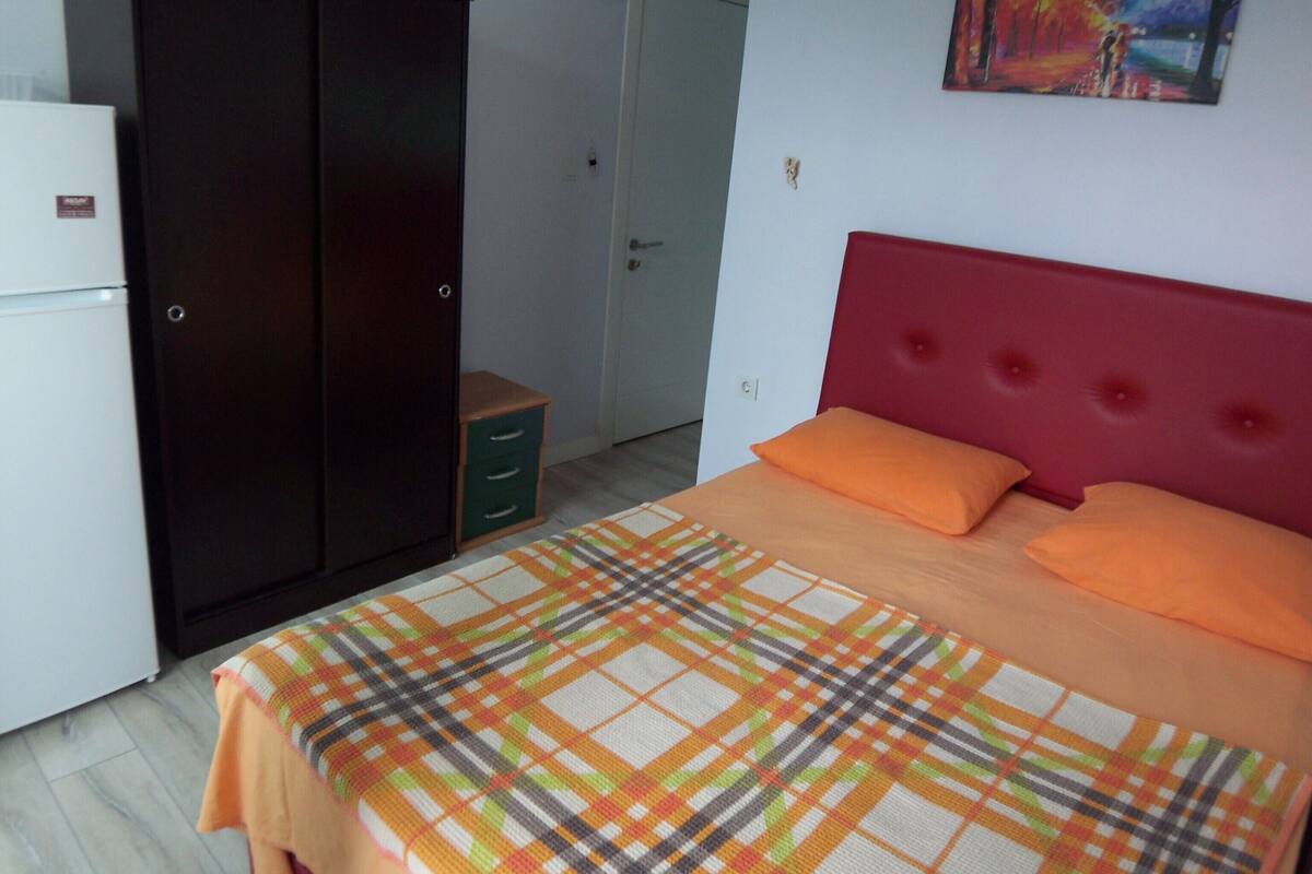 A bedroom with a bed, a wardrobe, a small cabinet, and a painting on the wall.
