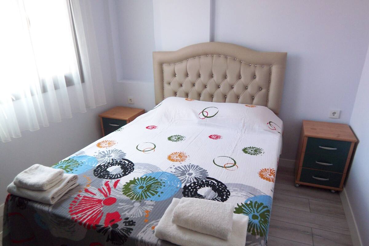 A neatly made bed with a floral-patterned bedspread and two folded towels on the footboard.