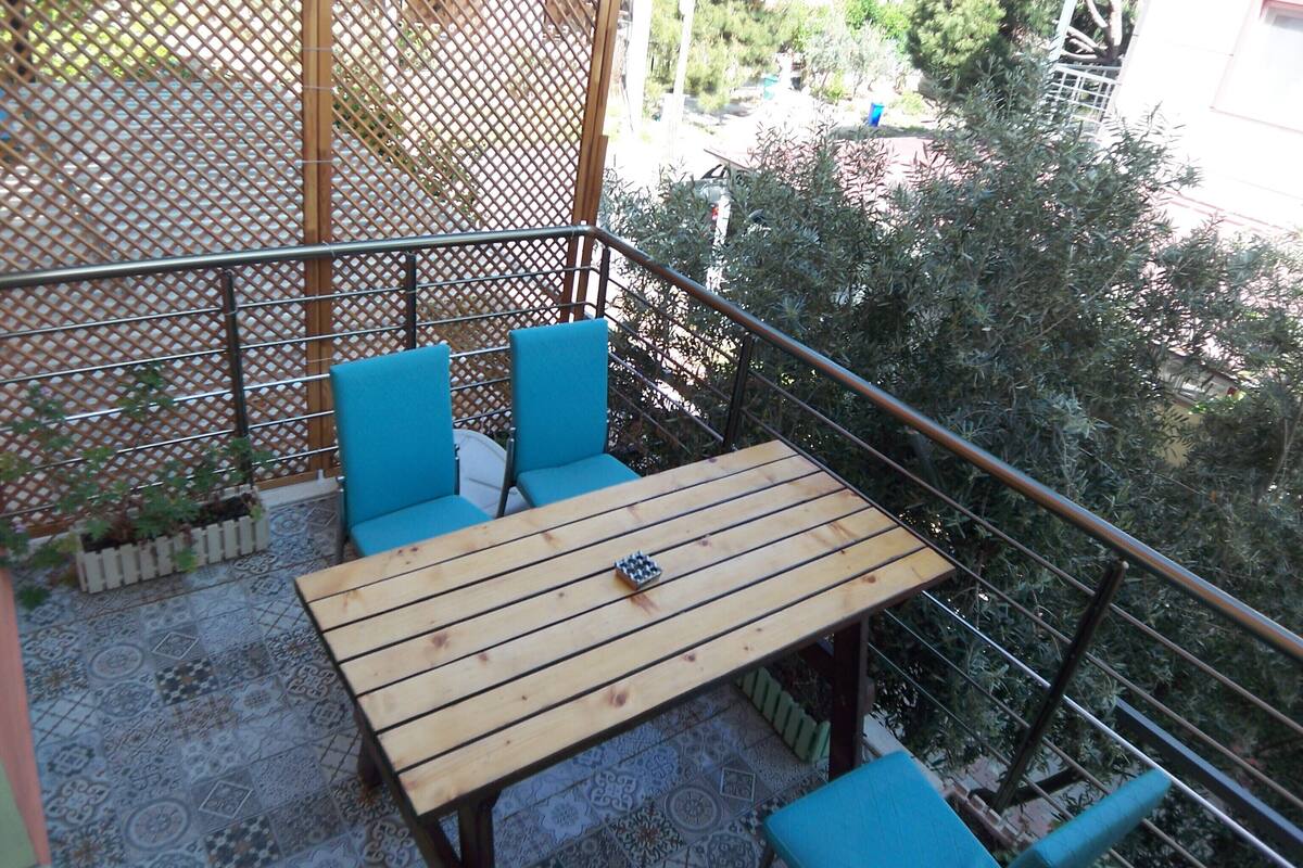 A wooden table with two blue chairs, a metal railing, and a patterned floor.