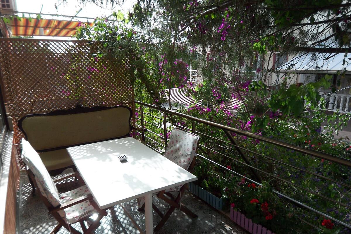 A balcony with a table and chairs, surrounded by a lattice fence and lush greenery.