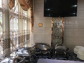 A buffet setup with multiple serving stations, a flat-screen TV mounted on the wall, and decorative curtains.