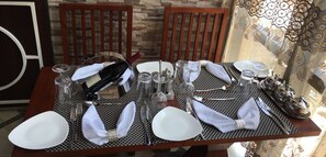 Mesa de comedor preparada para cuatro personas, con platos blancos, cubiertos y cristalería.