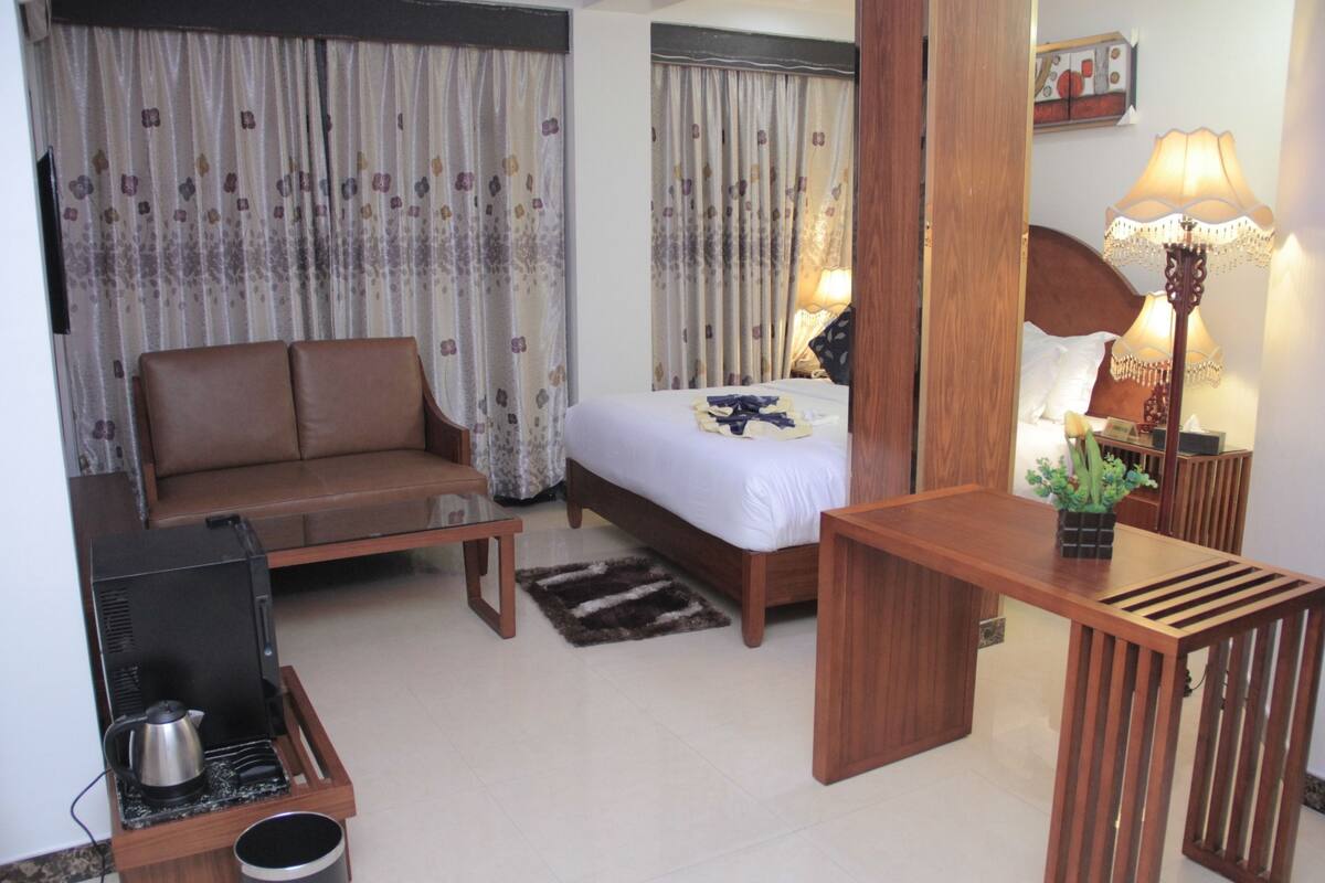 Ein Hotelzimmer mit Bett, Sofa, Schreibtisch, Lampe und Fernseher.