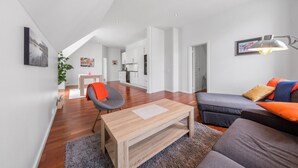 Ein modernes Wohnzimmer mit einem Holztisch, einem grauen Sofa mit orangefarbenen Kissen und einem grauen Sessel.
