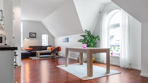 Ein großzügiger Wohnbereich mit Holzboden, einem Esstisch, einer Couch und einem großen Fenster, das für natürliches Licht sorgt.